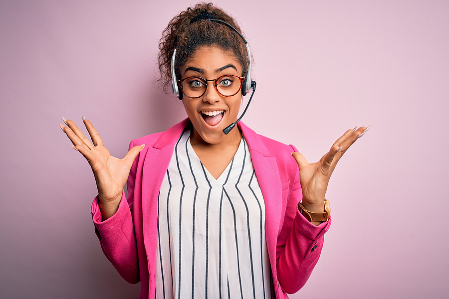 Young african american call center agent girl wearing glasses working using headset celebrating crazy and amazed for success with arms raised and open eyes screaming excited. Winner concept