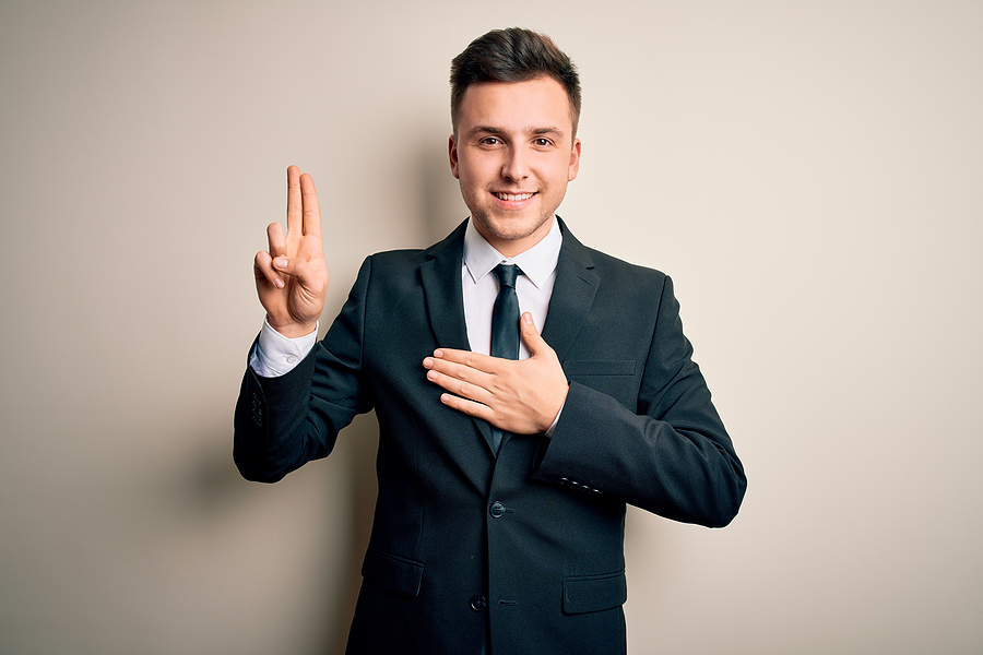 Young handsome business man wearing elegant suit and tie over isolated background smiling swearing with hand on chest and fingers up, making a loyalty promise oath